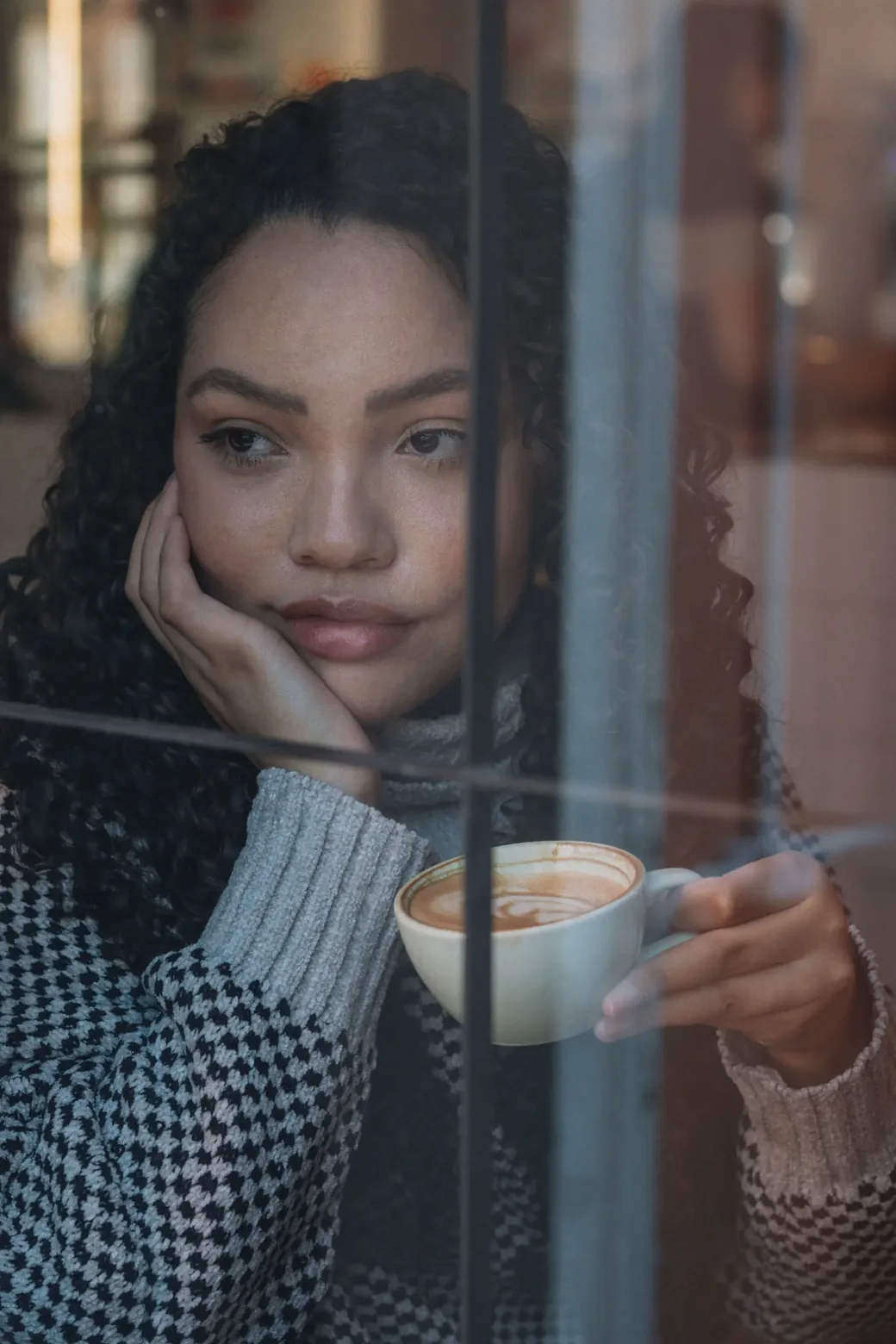 Mujer latina pensativa junto a la ventana, sosteniendo una taza de café